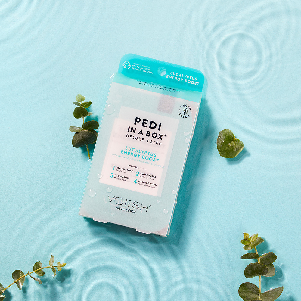 VOESH New York Pedi in a Box Deluxe 4 Step Eucalyptus Energy Boost Fußpflege-Set mit Eukalyptus auf blauem Wasserhintergrund mit Blättern und Wassertropfen