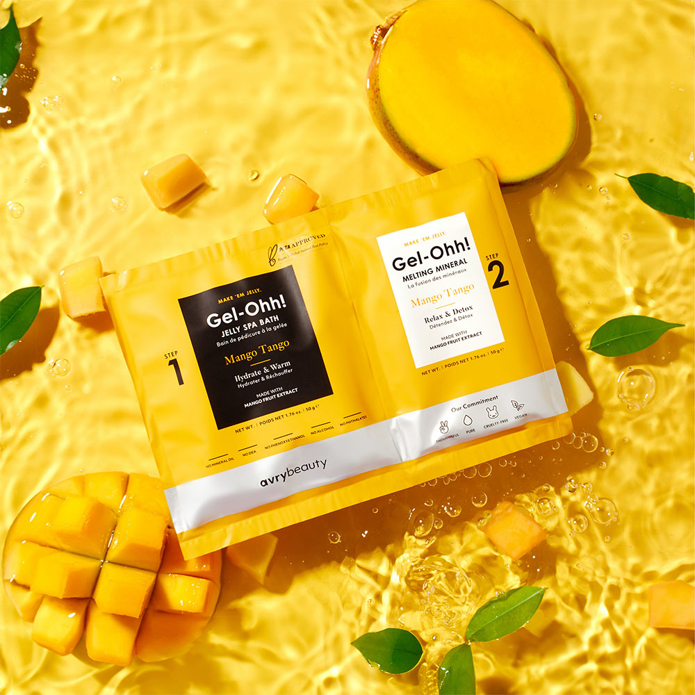 Gel-Ohh! Mango Tango Fußbad-Set von avrybeauty mit Jelly Spa Bath und Melting Mineral, inszeniert mit Mango, Mangostücken und Blättern im gelben Wasser