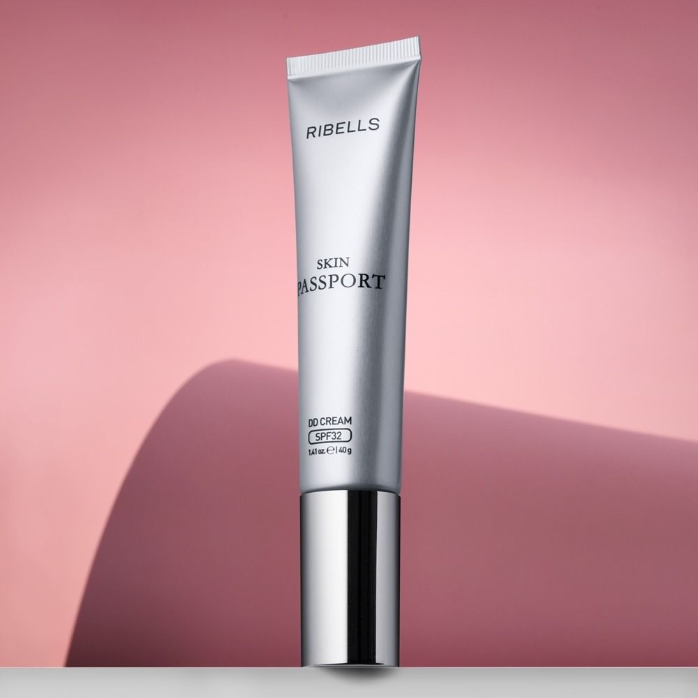 RIBELLS Skin Passport DD Cream SPF 32 in silberner Tube vor rosa Hintergrund, getönte Tagespflege mit Sonnenschutz für das Gesicht