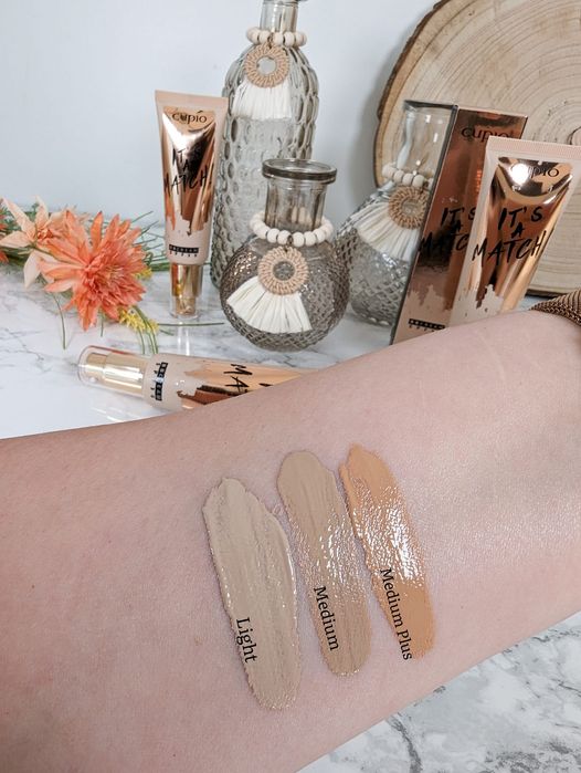 343515937_782063283286486_6703323425866600347_n Drei verschiedene Make-up-Schattierungen, Light, Medium und Medium Plus, auf einem Arm mit dekorativen Flaschen im Hintergrund
