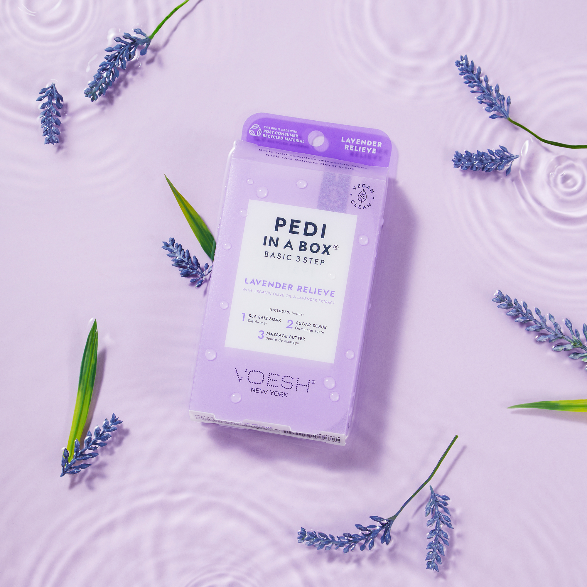 VOESH Pedi In A Box Basic 3 Step Lavender Relieve Pediküre-Set, umgeben von Lavendelzweigen auf lilafarbenem Hintergrund mit Wasserwellen