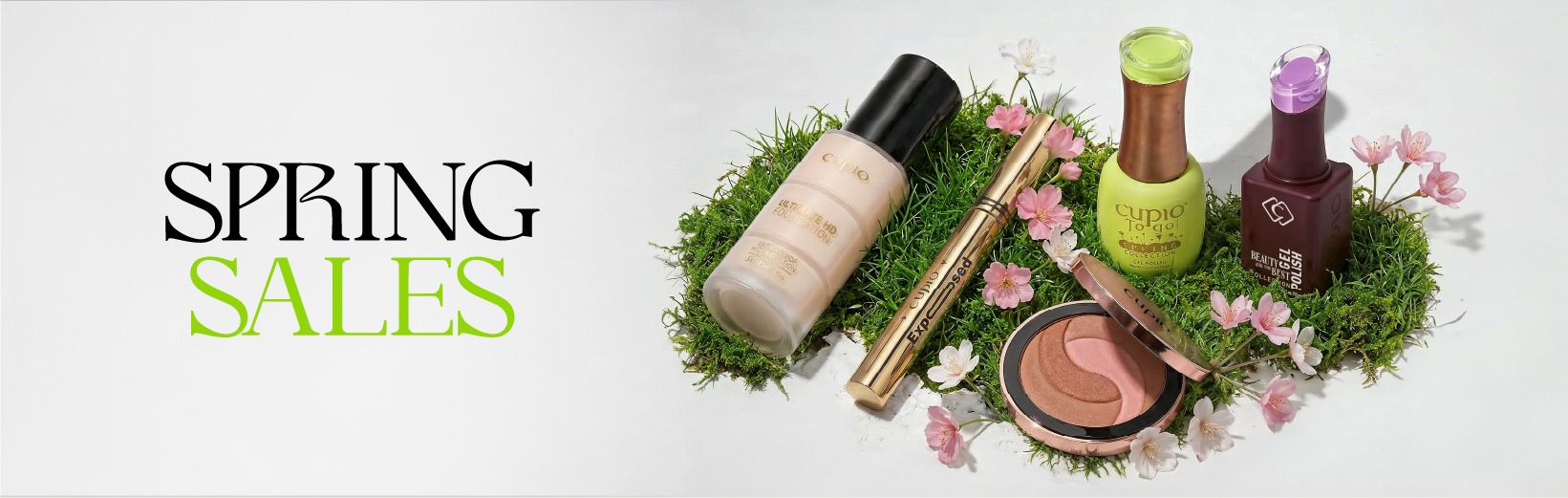 Werbebanner Frühlingssale mit dekorativen Kosmetikprodukten: Foundation, Mascara, zwei Nagellacke und Rouge auf grünem Moos mit rosa Blüten