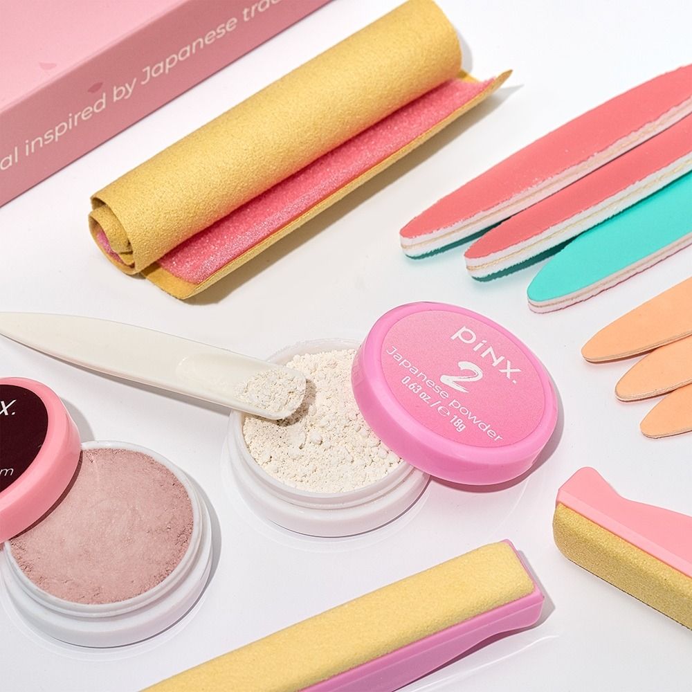 Nahaufnahme von PINK2 Nageldesign-Zubehör: offenes japanisches Pulver, Feilen, Polierblöcke und Schleifhilfen in Rosa, Gelb und Mint