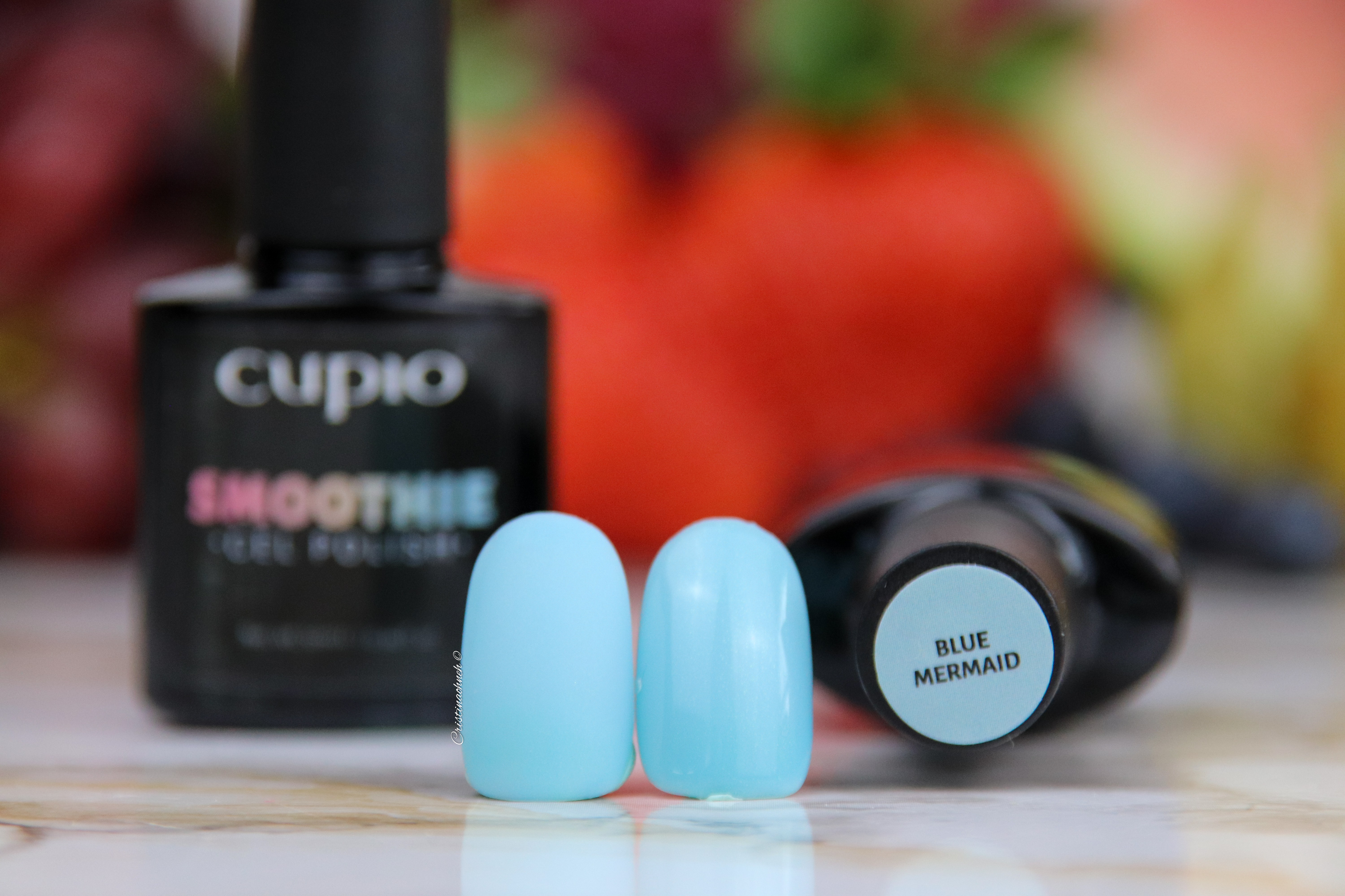 bluemermaid Zwei künstliche Nägel in Blau neben einer Flasche Cupio Smoothie Gel Polish in der Farbe Blue Mermaid.