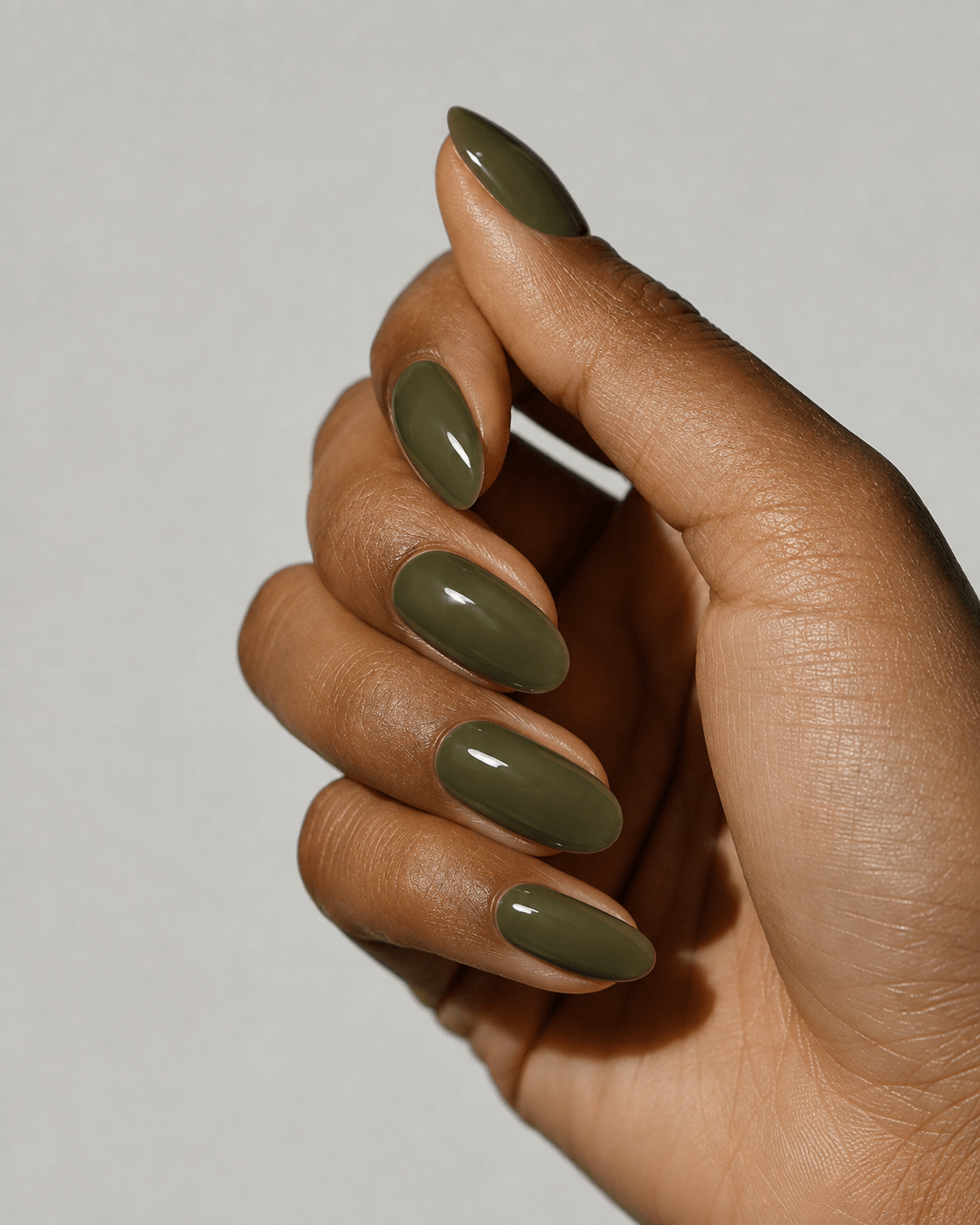 Nahaufnahme einer Hand mit olivgrünen, mandelförmigen Kunstnägeln in glänzendem Finish
