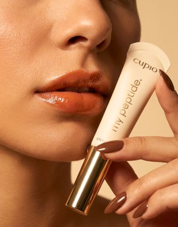 Frau hält Cupio Lily Popride Lippenprodukt an die Lippen, glänzender Nude-Look in Nahaufnahme