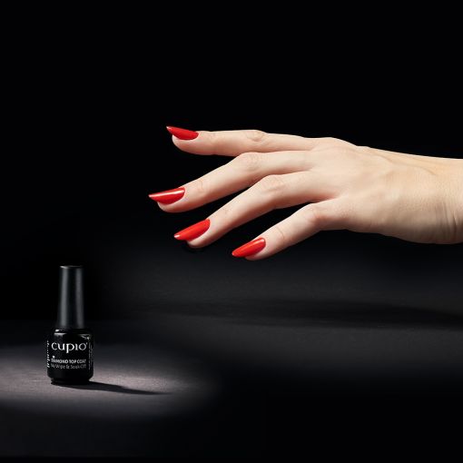 diamond_top_coat_1 Hand mit roten Nägeln greift nach einem Fläschchen Cupio Nagellack