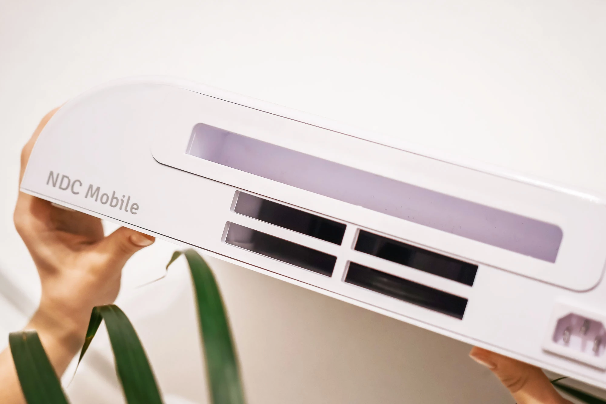 Mobile-plus-5b NDC Mobile Gerät, präsentiert von einer Person mit grüner Pflanze im Hintergrund