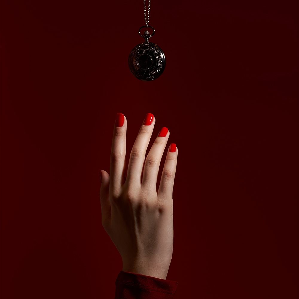 Nahaufnahme einer Hand mit rotem Nagellack, die eine schimmernde Taschenuhr an einer Kette erreicht