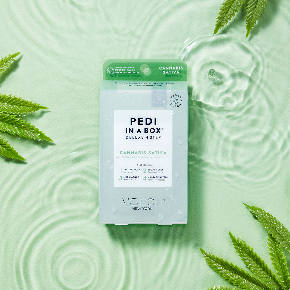 VOESH Pedi in a Box Deluxe 4 Step Cannabis Sativa Fußpflege-Set mit Sea Salt Soak, Sugar Scrub, Mud Masque und Massage Butter auf mintgrünem Wasserhintergrund mit Blättern