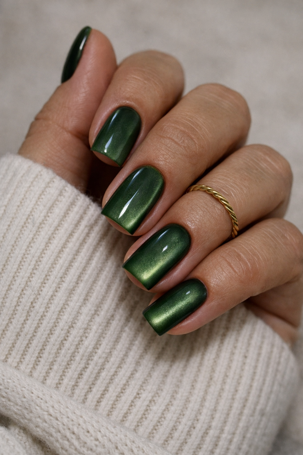 Hand mit grünem Metallic-Nagellack und Goldring