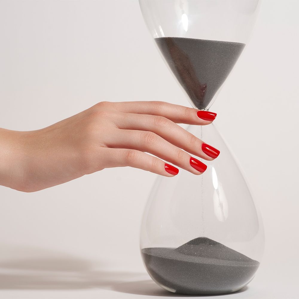 Nahaufnahme einer Hand mit roten Nägeln, die eine Sanduhr berührt