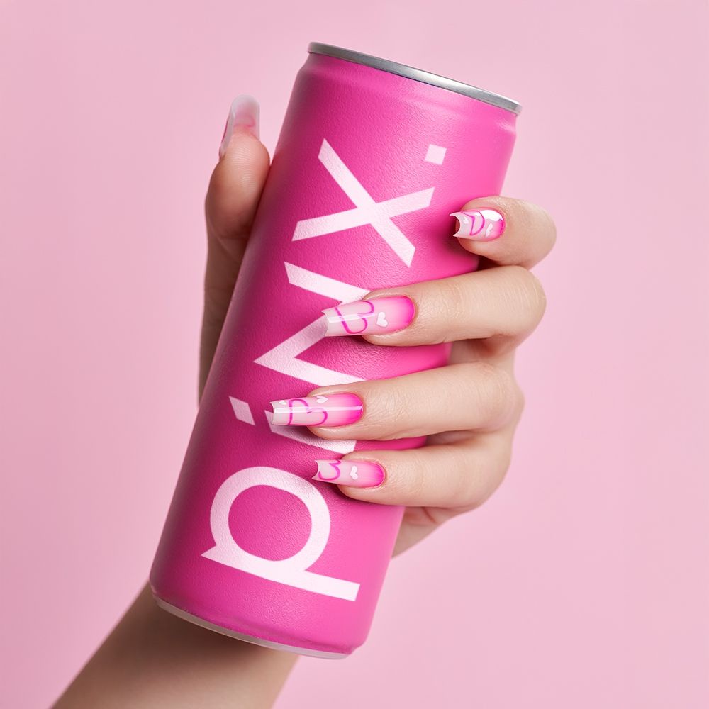 Hand hält eine pinke Getränkedose mit bunten Nägeln vor einem rosa Hintergrund