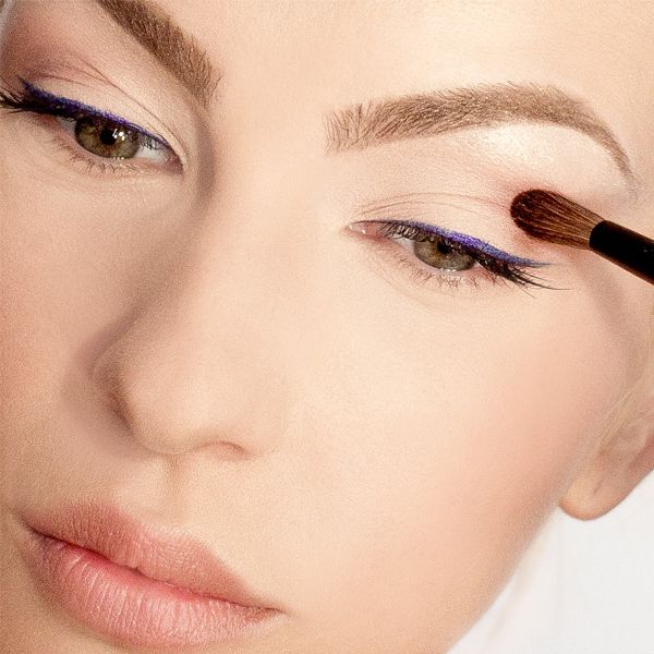 Frau mit lila Eyeliner trägt Make-up mit einem Pinsel auf