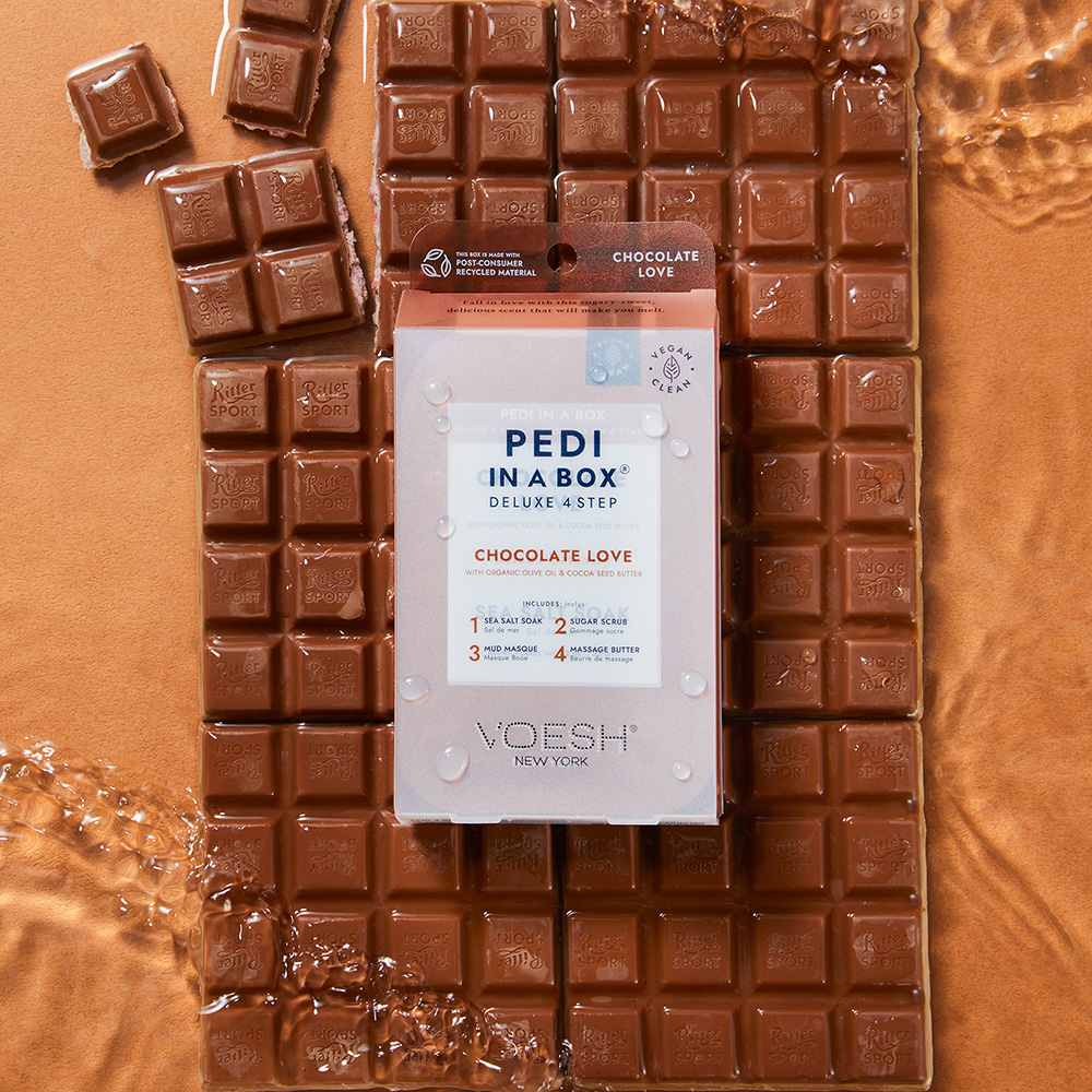VOESH Pedi in a Box Deluxe 4 Step Chocolate Love Pediküre-Set mit Schokoladenmotiv, platziert auf mehreren Schokoladentafeln
