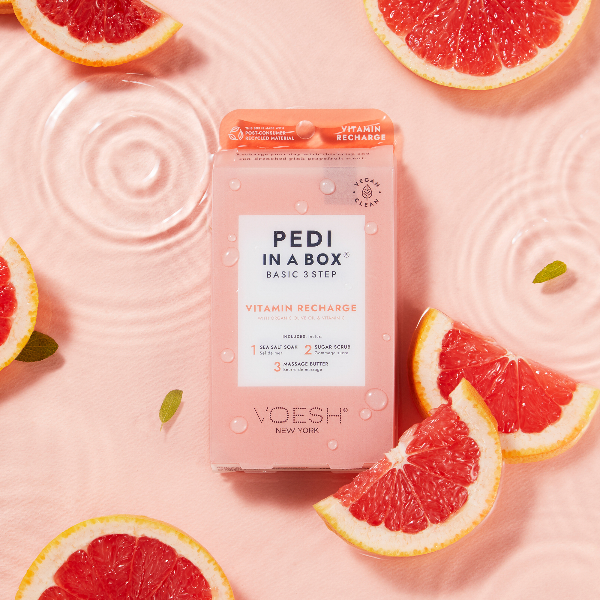 VOESH Pedi in a Box Basic 3 Step Vitamin Recharge Pediküre-Set, umgeben von Grapefruitscheiben auf rosa Hintergrund