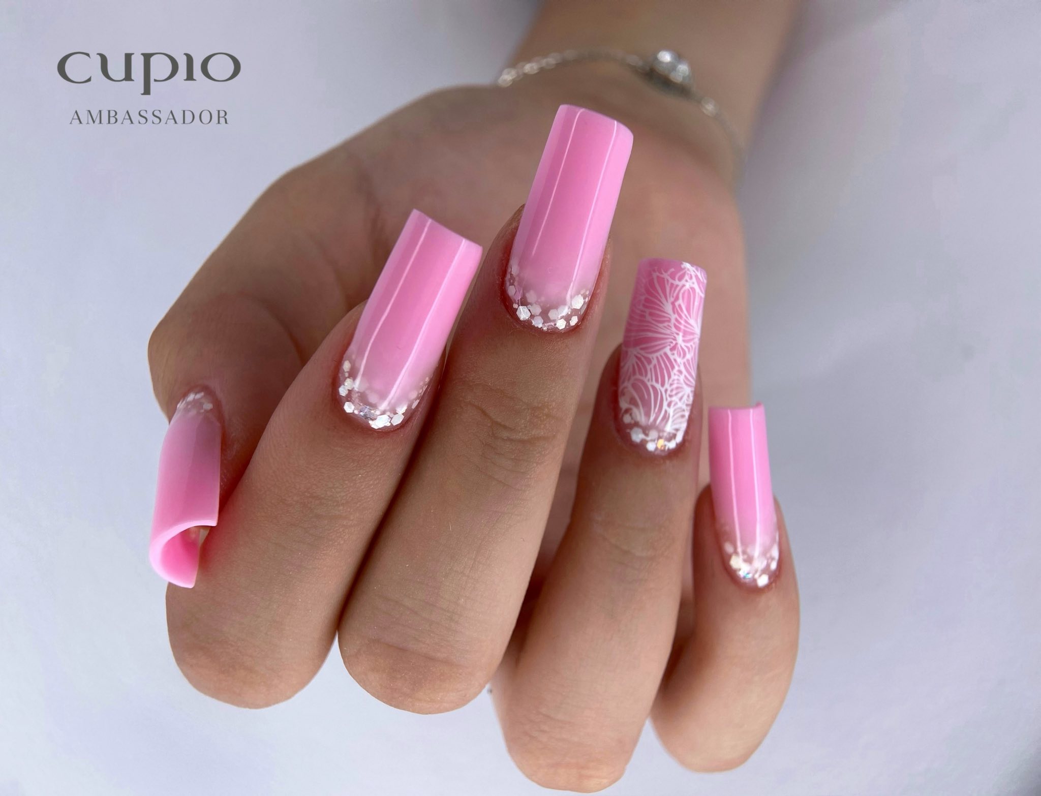 Händevorschau mit pinken Nägeln, verziert mit Glitzer und einem filigranen floralen Muster.