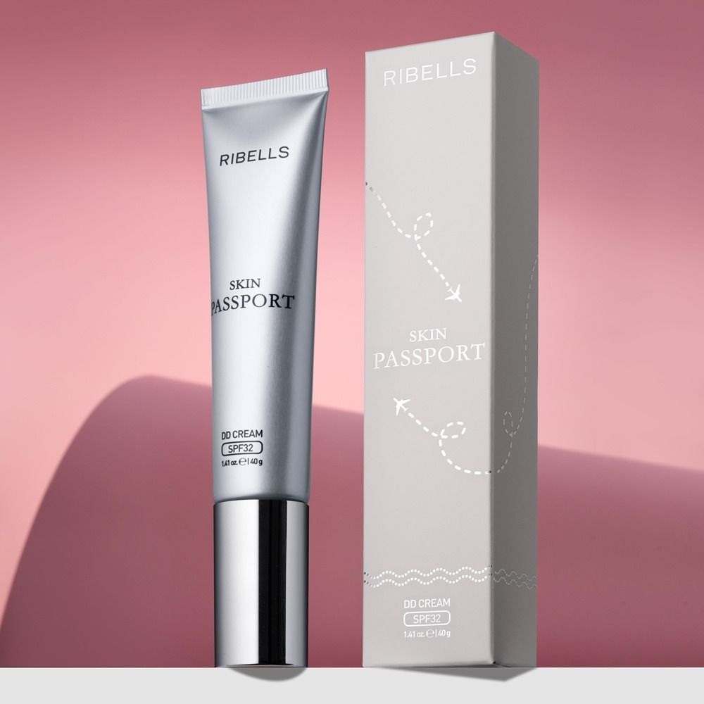 Produktfoto der RIBELLS Skin Passport DD Cream SPF32 in silberner Tube mit passender Faltschachtel vor rosafarbenem Hintergrund