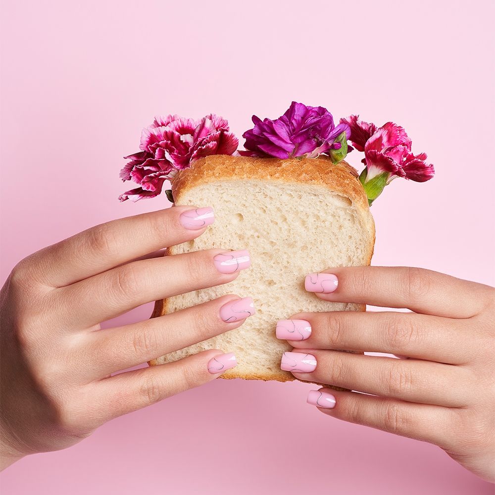 Frau hält ein Stück Brot mit bunten Blumen, auf pinkem Hintergrund