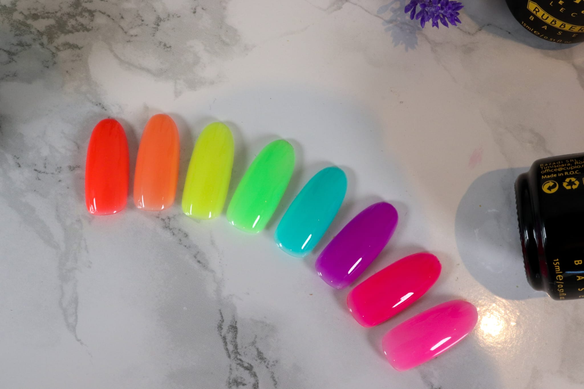 11 Neon-Nagellackfarben in orange, gelb, grün, blau, lila und pink auf einem marmorierten Untergrund