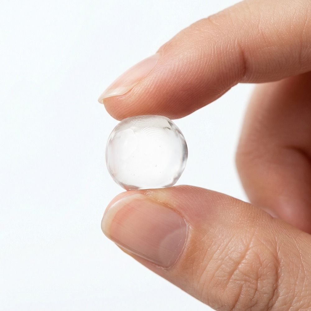 Nahaufnahme einer Hand, die eine kleine transparente Gel- oder Silikonkugel zwischen Daumen und Zeigefinger hält