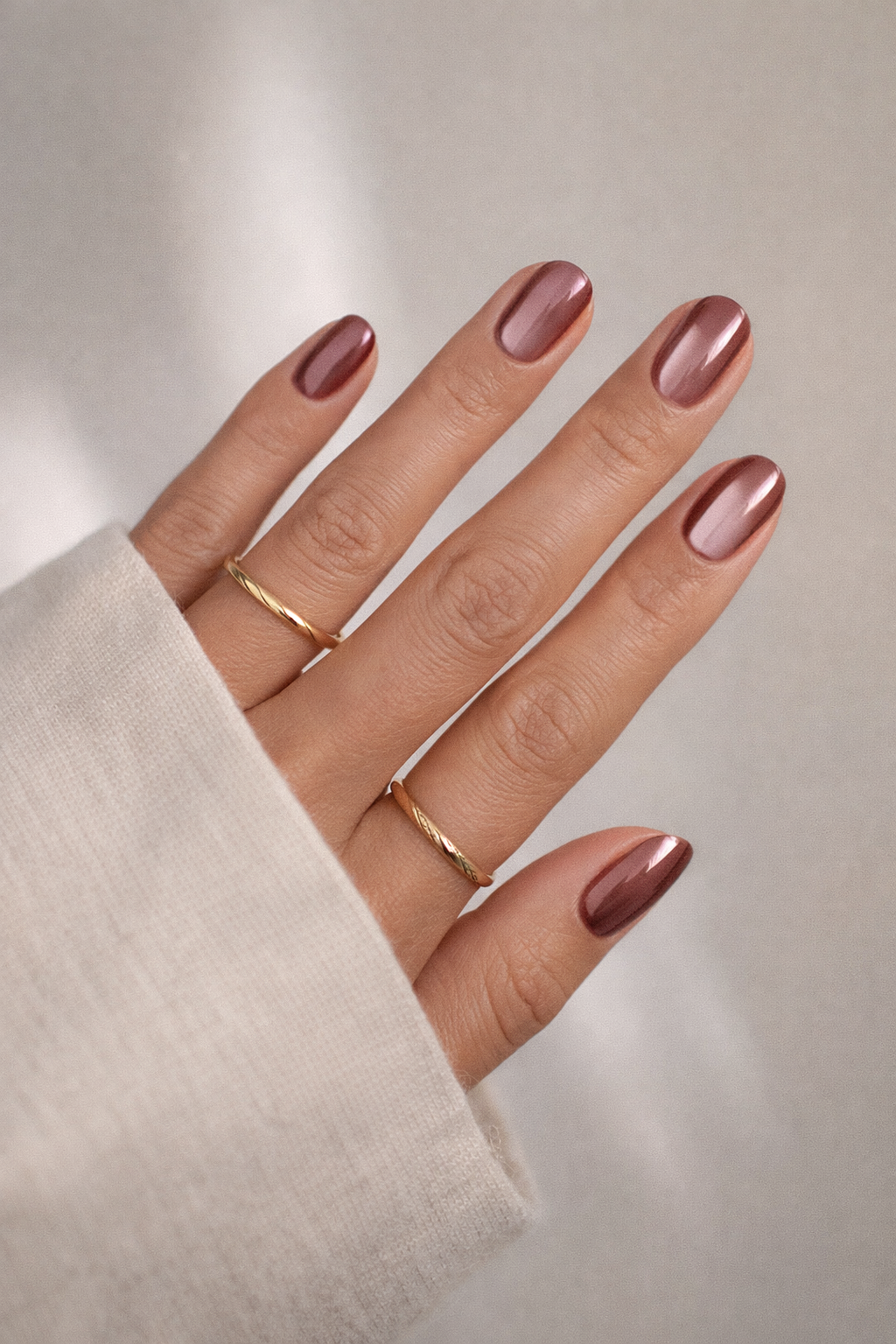 Hand mit roségolder Maniküre und filigranen Goldringen