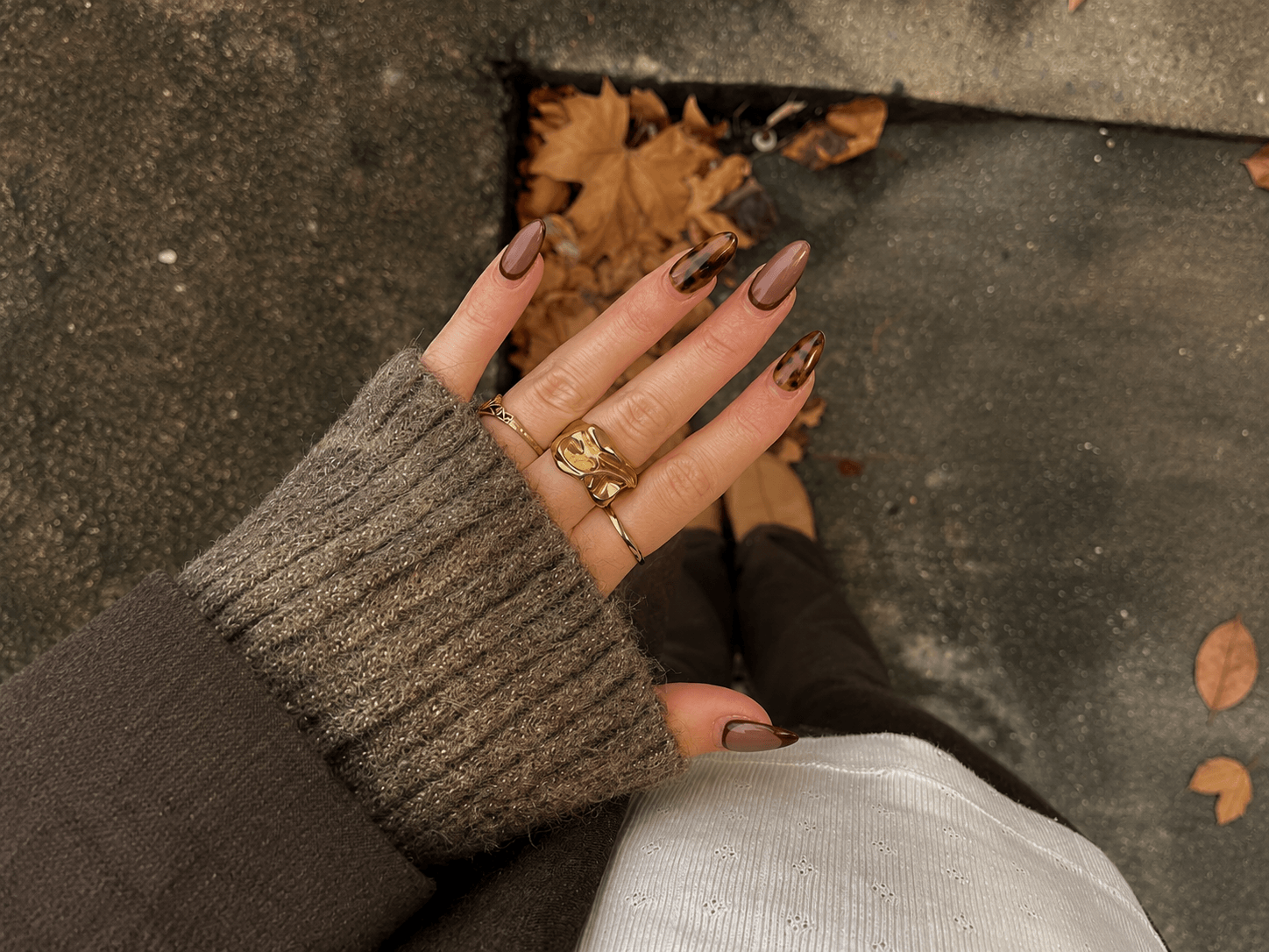 Hand mit braunen Press-on Nails in Mandelform, glänzendem Herbstlook und Leo-Muster als Produktansicht im Alltag