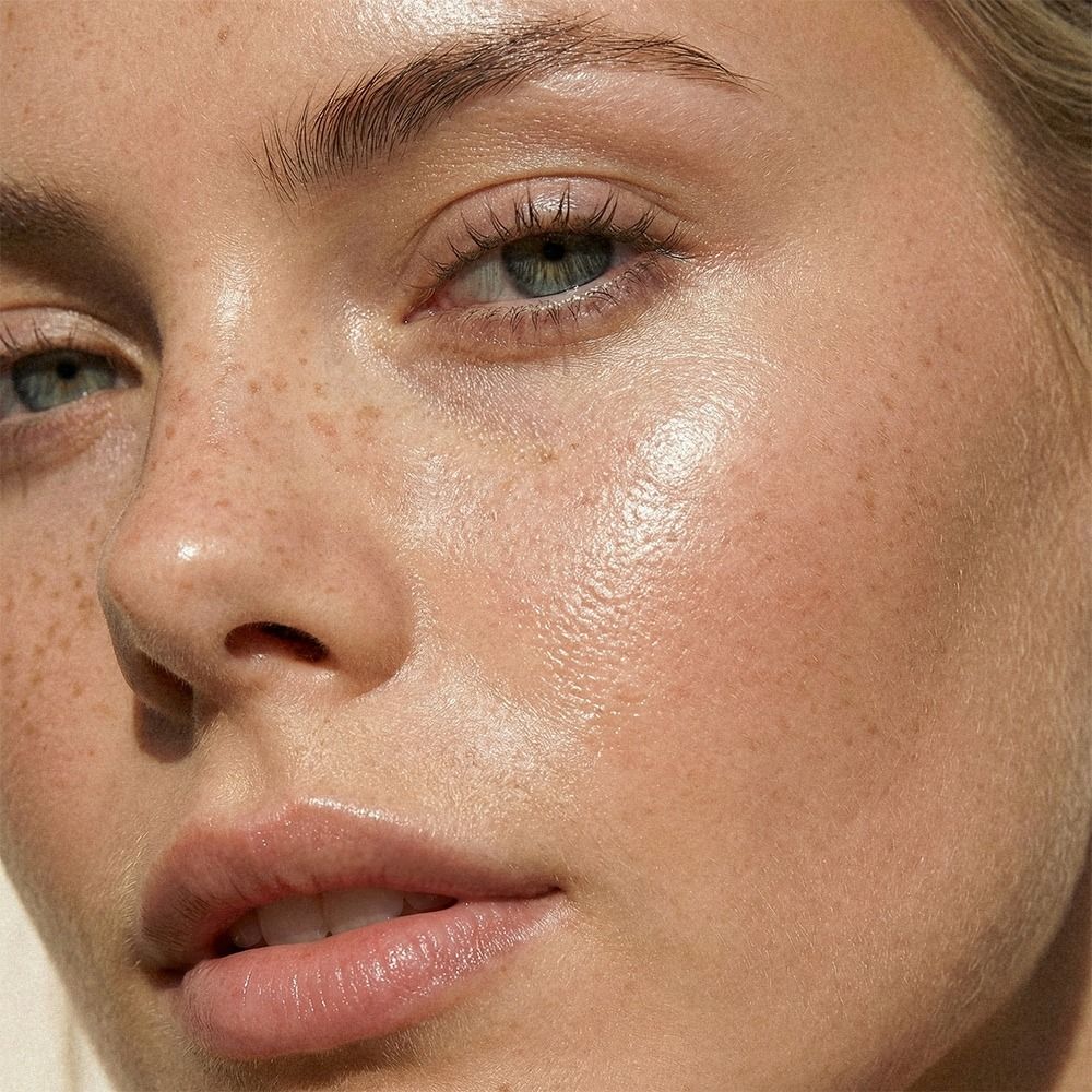 Detailaufnahme eines weiblichen Gesichts mit glatter, glänzender Haut und leichten Sommersprossen als Ergebnis intensiver Gesichtspflege