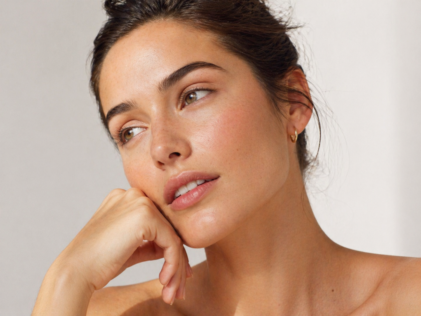 Porträt einer Frau mit strahlender Haut und kleinem goldfarbenem Creolen-Ohrring als stilvolles Schmuckdetail