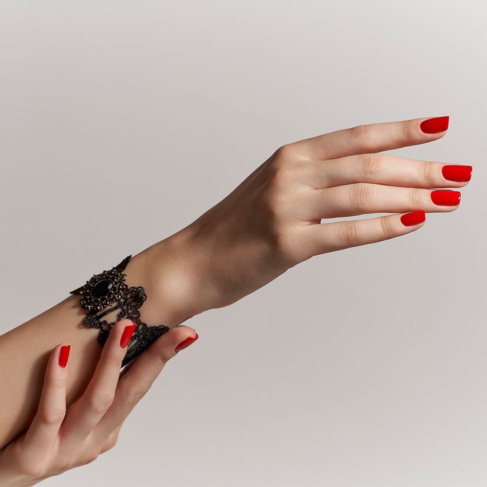 Schöne Hände mit rotem Nagellack und schwarzem Schmuckarmband auf neutralem Hintergrund