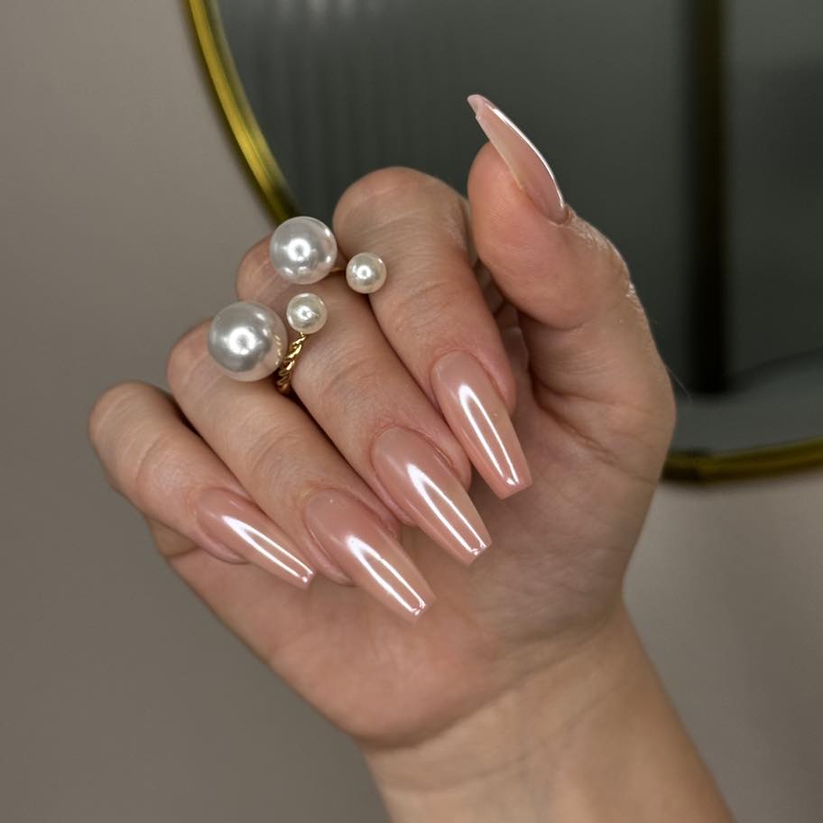 Nahaufnahme einer Hand mit langen, glänzenden, spitzen Nägeln und einem Ring mit Perlen