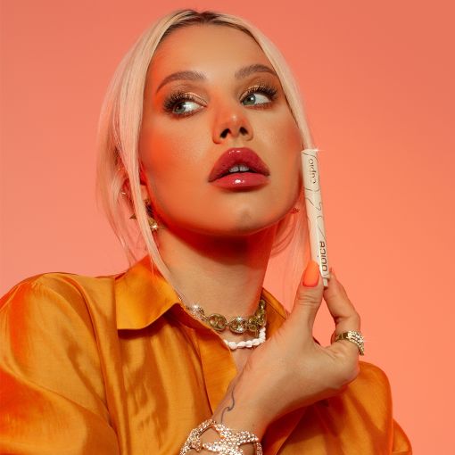 mg_0869_1_ Frau hält einen Lippenstift in der Hand und posiert vor einem orangefarbenen Hintergrund