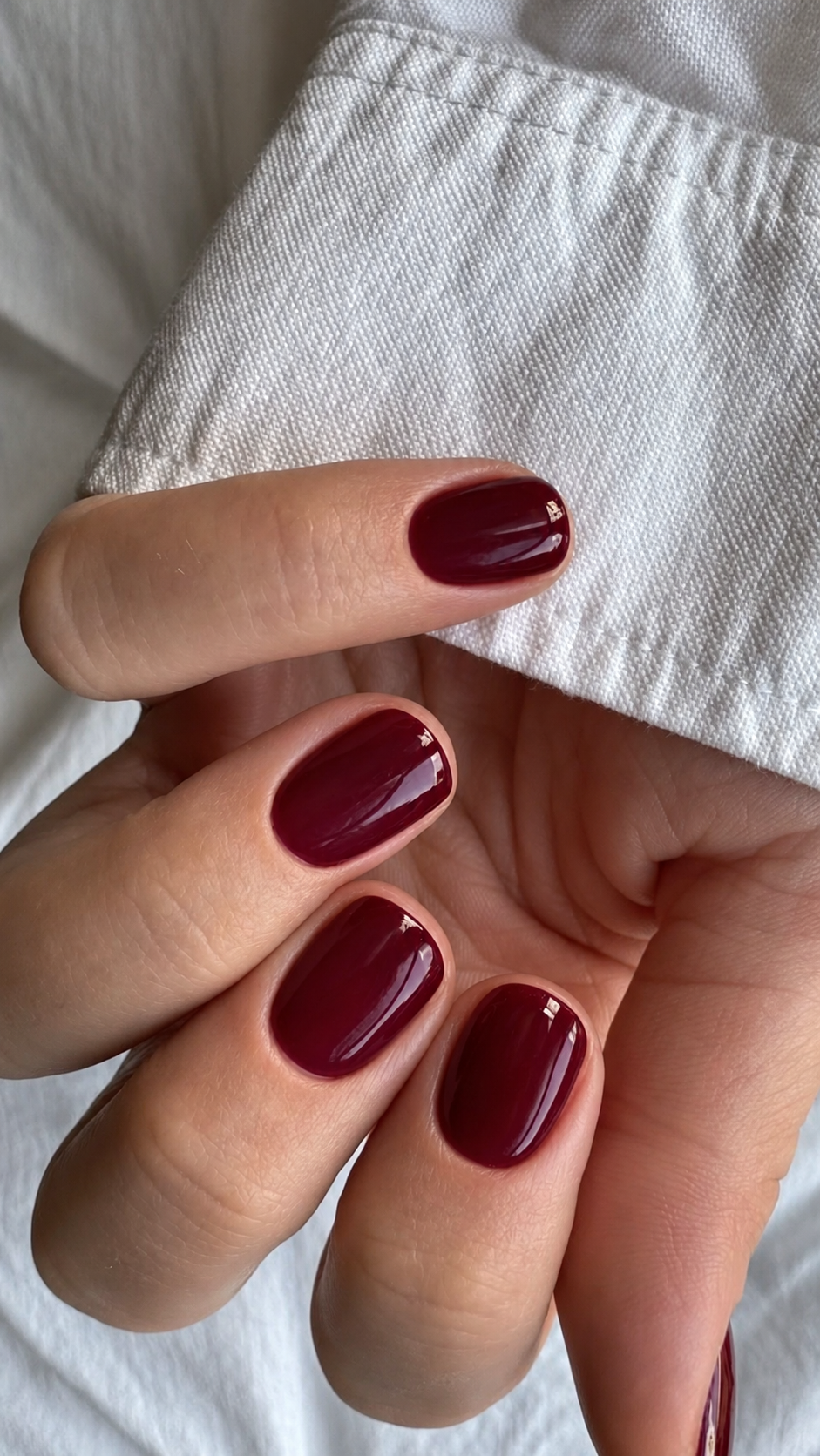 Nahaufnahme einer Hand mit kurzen, ovalen Nägeln in bordeauxroter Gel-Maniküre mit glänzendem Finish