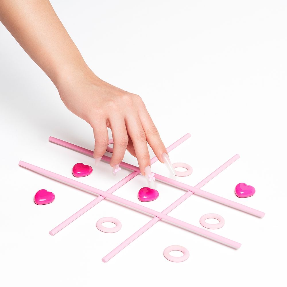 Händchen, das ein pinkes Herz im Tic Tac Toe Spiel platziert
