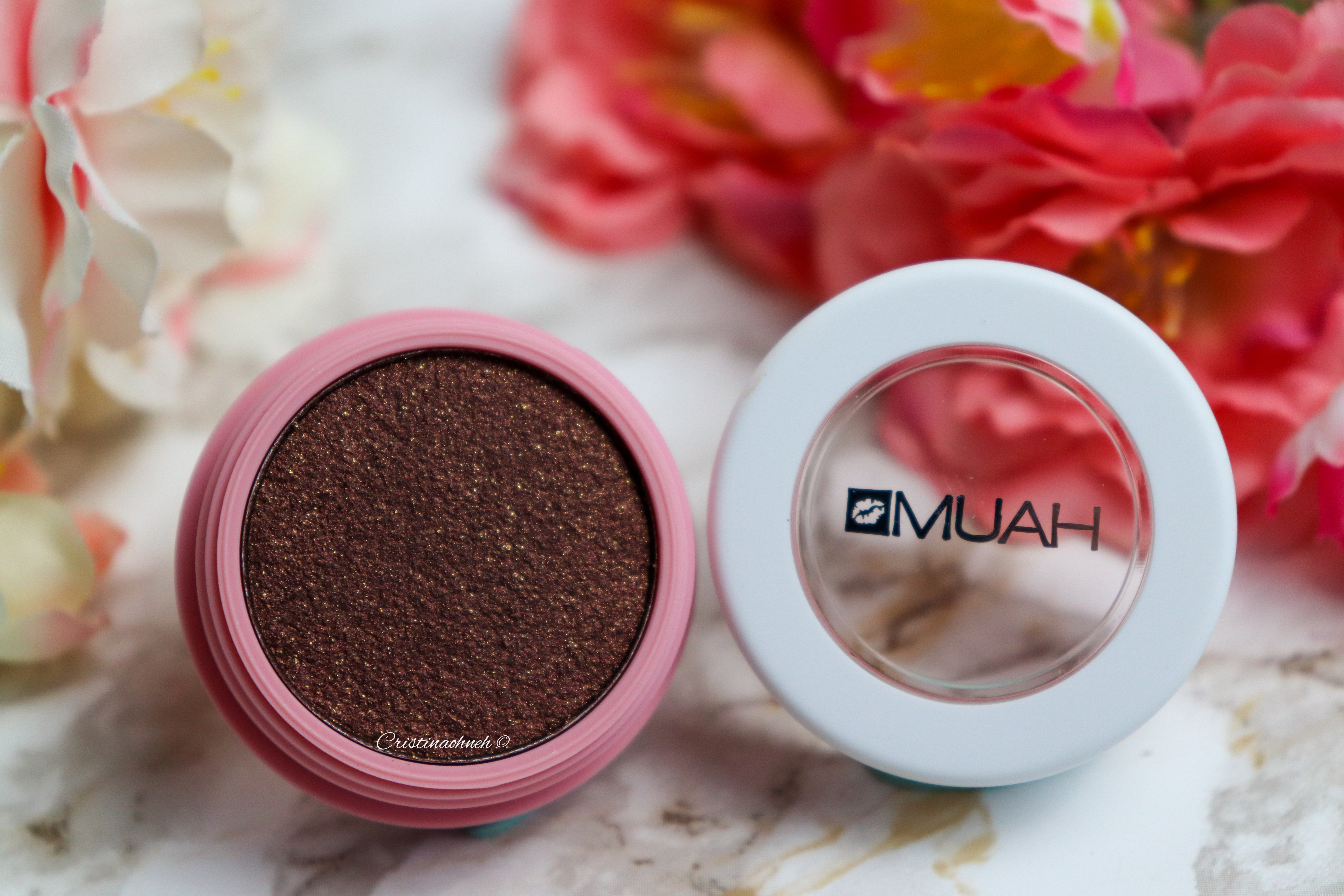 Dunkelbrauner Lidschatten in einem runden Behälter von MUAH, umgeben von Blumen.