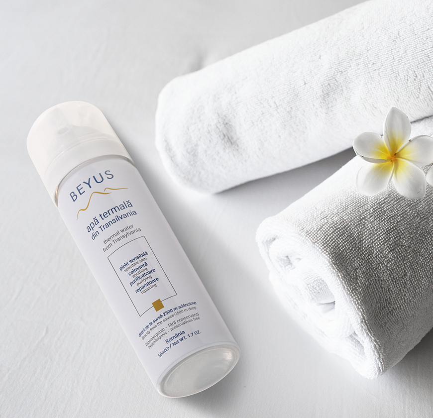 BEYUS Thermalwasser in der Flasche mit Handtüchern und Blüte im Hintergrund