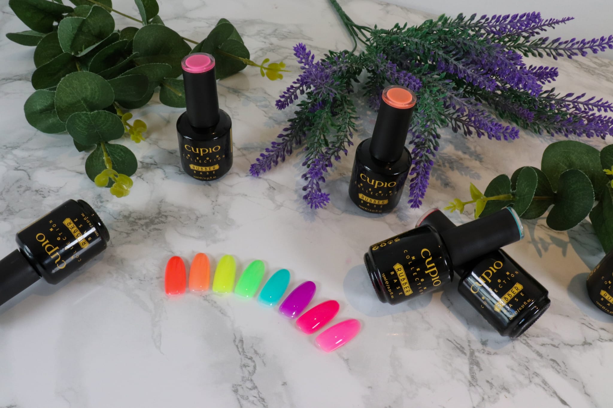 12 Farbenfrohe Gel-Nagellacke von Cupio sowie farbige Nagelspitzen auf marmoriertem Hintergrund.