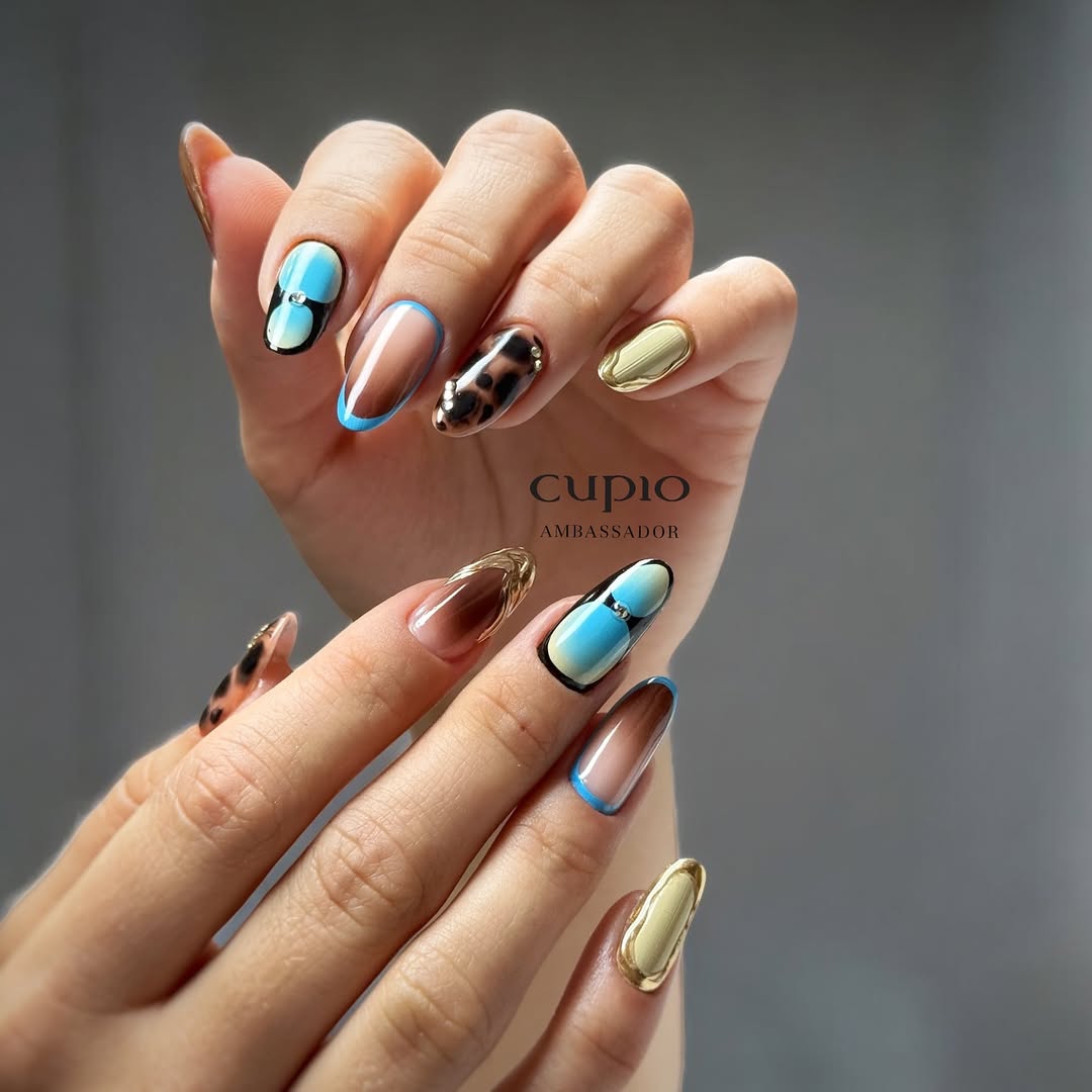 Hände mit kreativ gestalteten Nägeln in verschiedenen Farben, darunter Blau, Gold und Zebra-Muster.