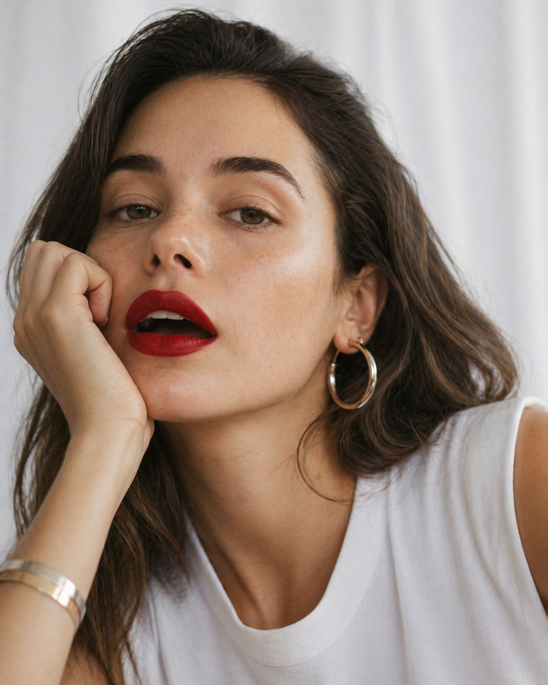 Nahaufnahme einer Frau mit goldfarbenen Creolen und Armreif, rotem Lippenstift und weißem Top – Schmuck im modischen Look