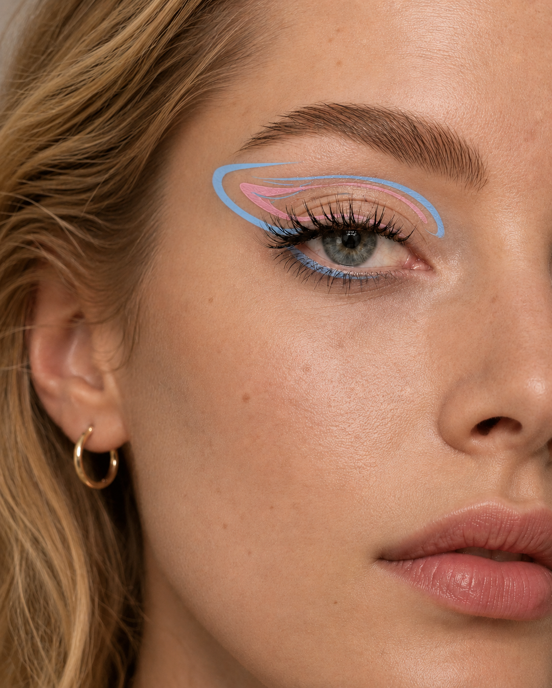 Detailaufnahme eines weiblichen Gesichts mit blau-rosafarbenem grafischem Eyeliner am Oberlid und unter dem Auge