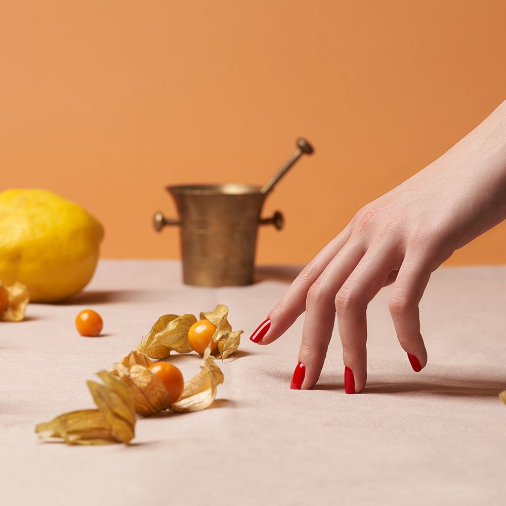 Hand mit roten Nägeln greift nach dekorativen Früchten auf einem Tisch