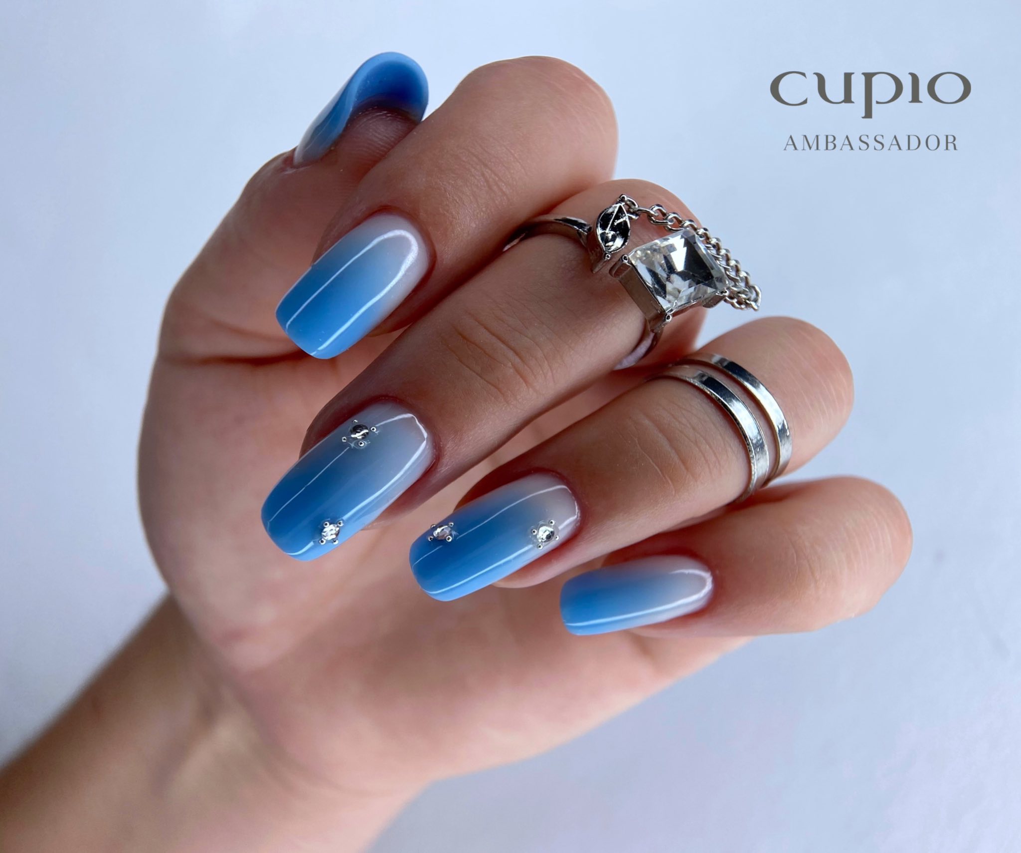 Hübsche Nägel mit sanftem Blauton und Schmuck auf der Hand