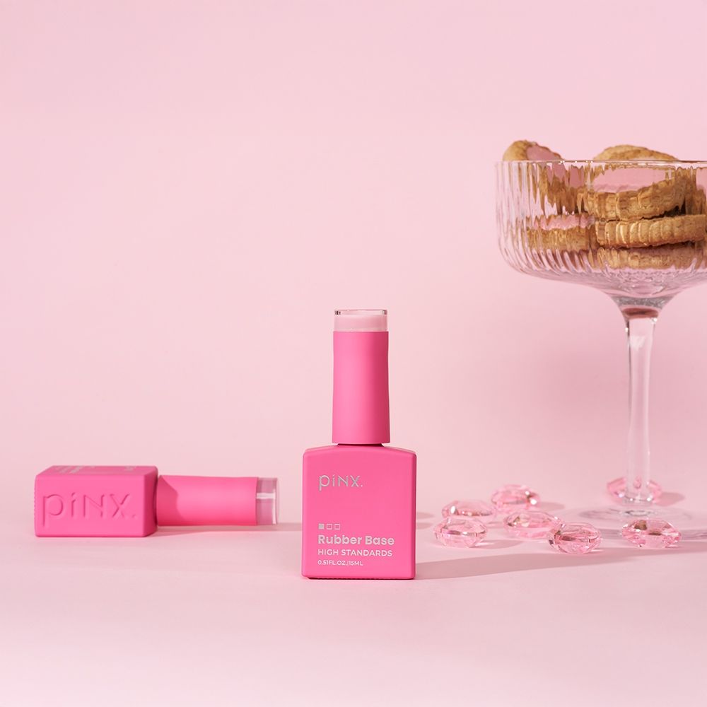 Flasche mit pinkem Rubber Base Nagellack von piNX neben einem Glas mit Keksen
