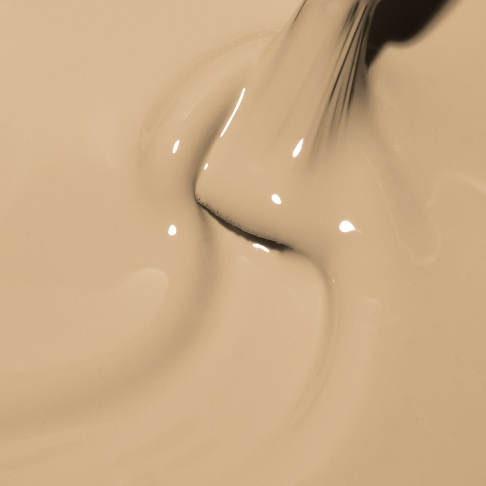 Makroaufnahme einer flüssigen Foundation in warmem Beige, die mit einem Make-up-Pinsel sanft verblendet wird